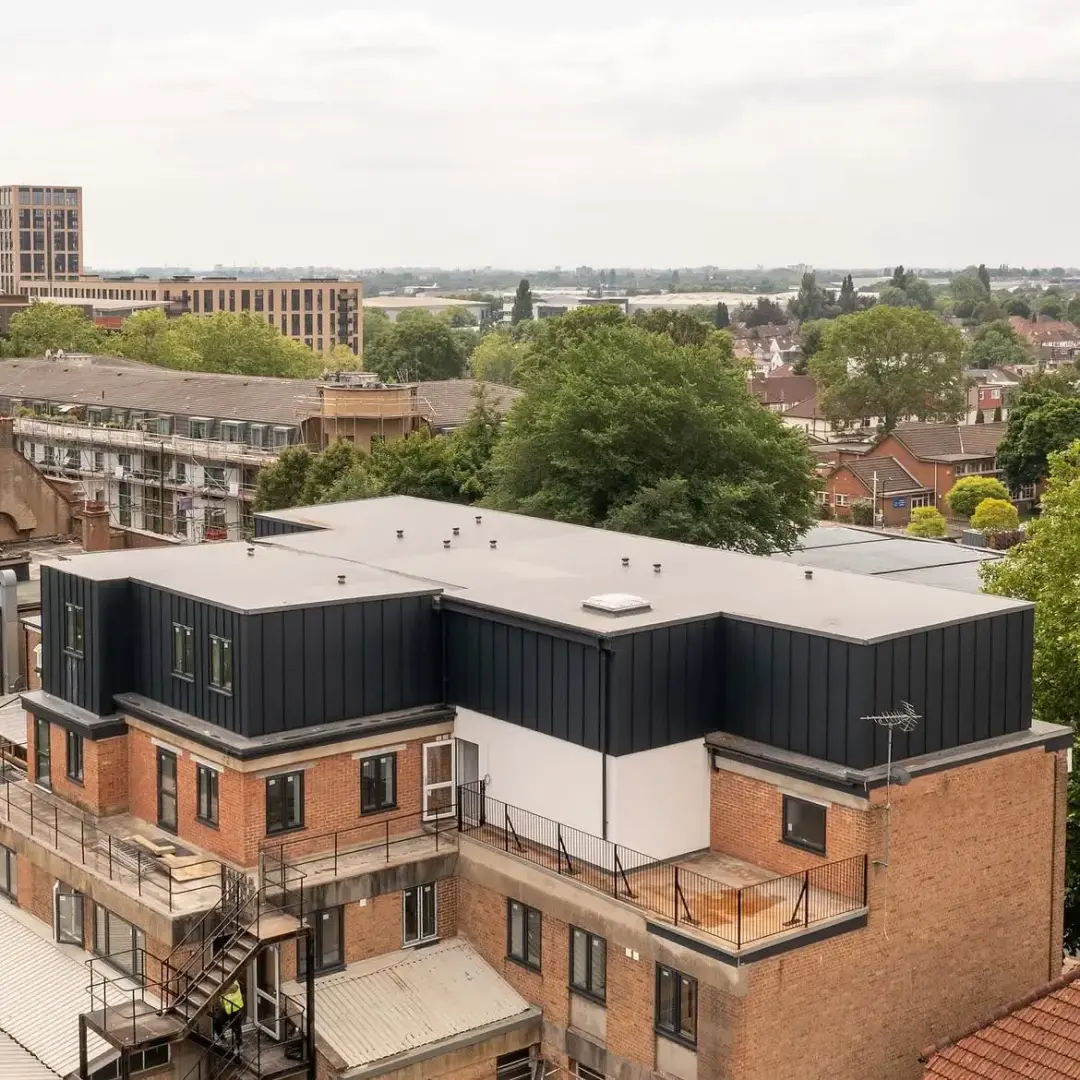 Dark vertical metal cladding above a brick building and terrace